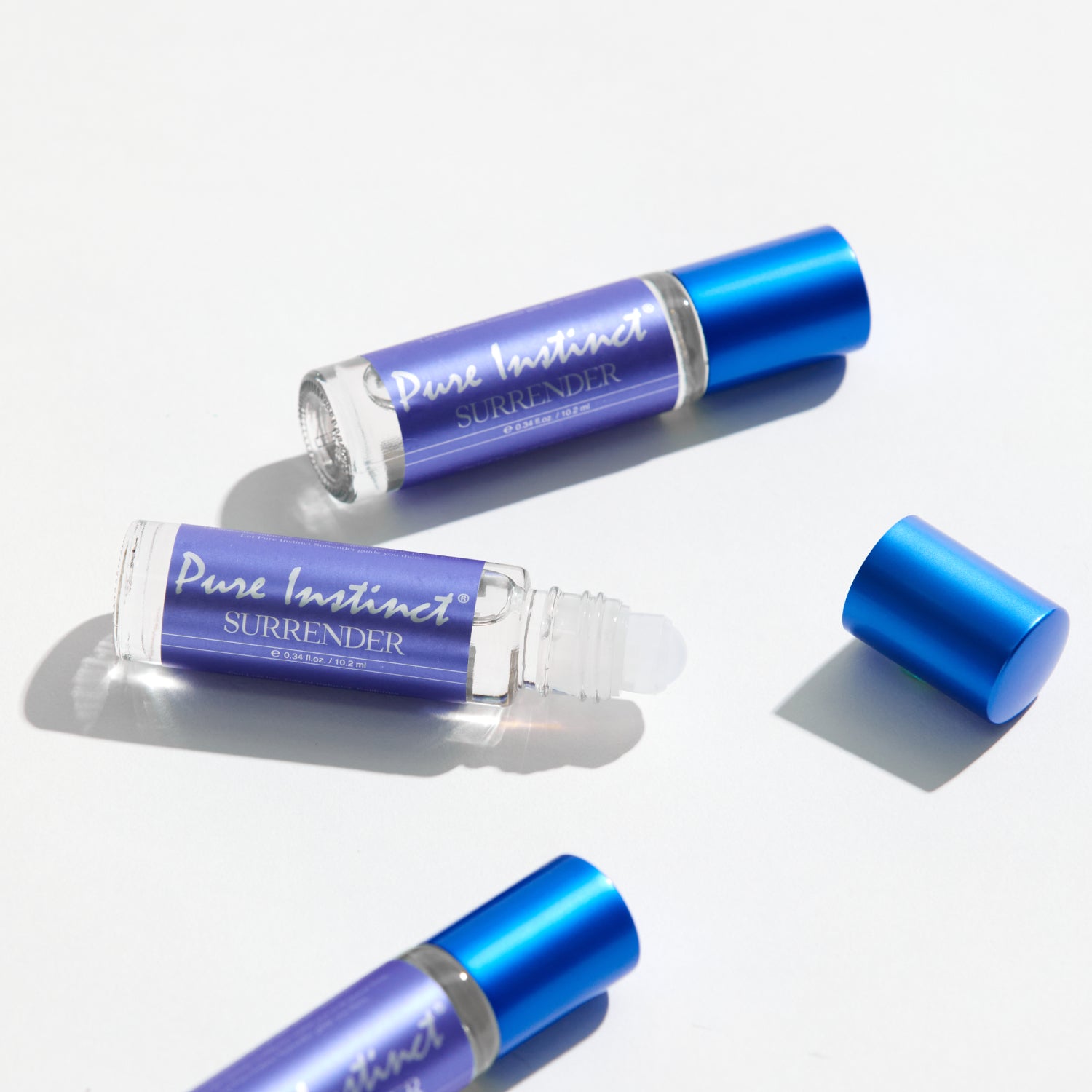 Surrender Roll-On Pheromone Perfume Oil bottles arranged on a white surface with one opened to display the roll-on applicator
