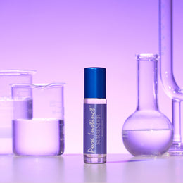 Surrender Roll-On Pheromone Perfume Oil standing among scientific beakers and flasks under a violet glow, highlighting a clean and sophisticated vibe