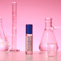 Pure Instinct FALLEN roll-on pheromone perfume oil standing among pink-tinted laboratory beakers and glassware