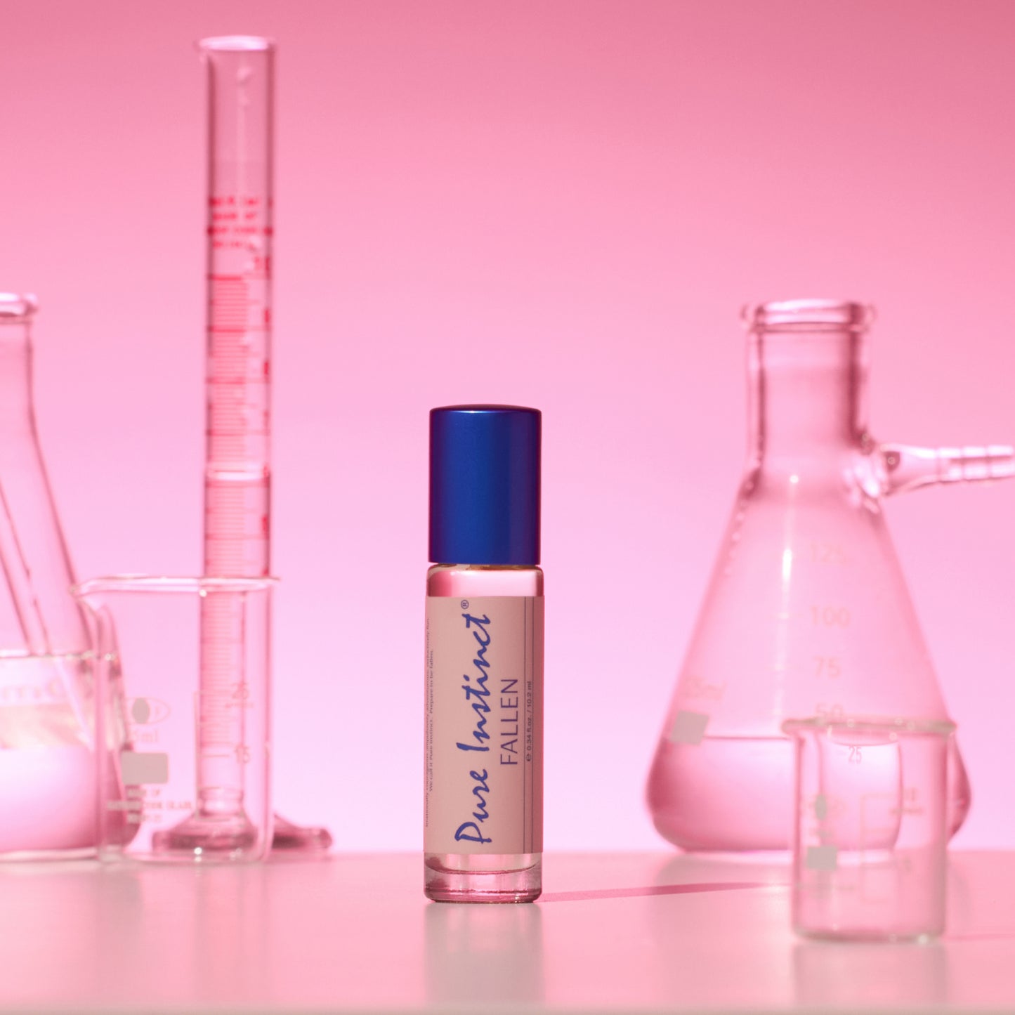 Pure Instinct FALLEN roll-on pheromone perfume oil standing among pink-tinted laboratory beakers and glassware
