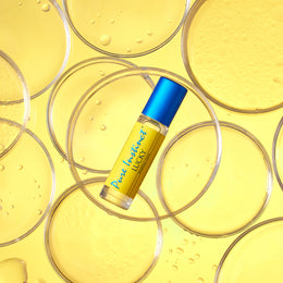 Lucky Roll-On Pheromone Perfume Oil placed among overlapping clear petri dishes filled with golden liquid on a bright yellow backdrop.