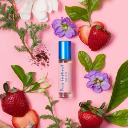 Pure Instinct FALLEN roll-on pheromone perfume oil surrounded by fresh strawberries, white flowers, and green leaves on a pink backdrop