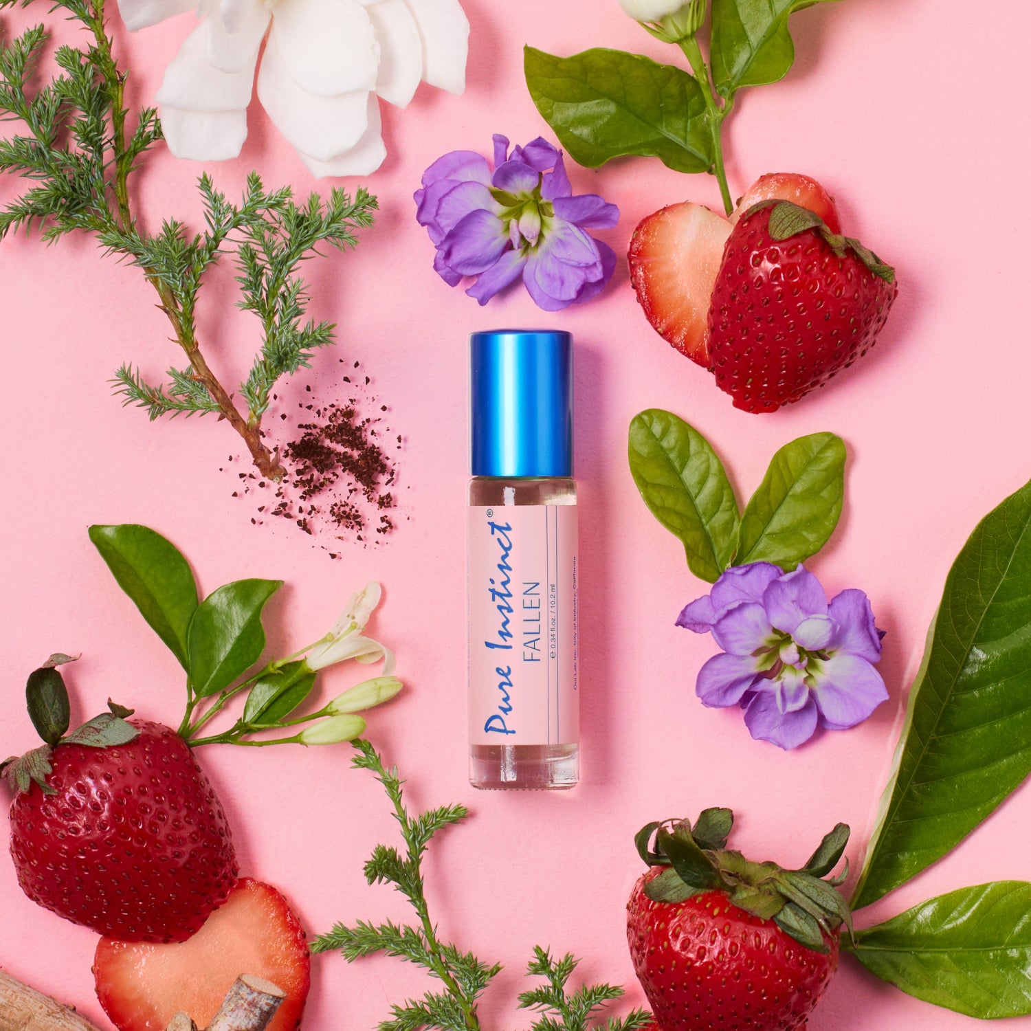 Pure Instinct FALLEN roll-on pheromone perfume oil surrounded by fresh strawberries, white flowers, and green leaves on a pink backdrop