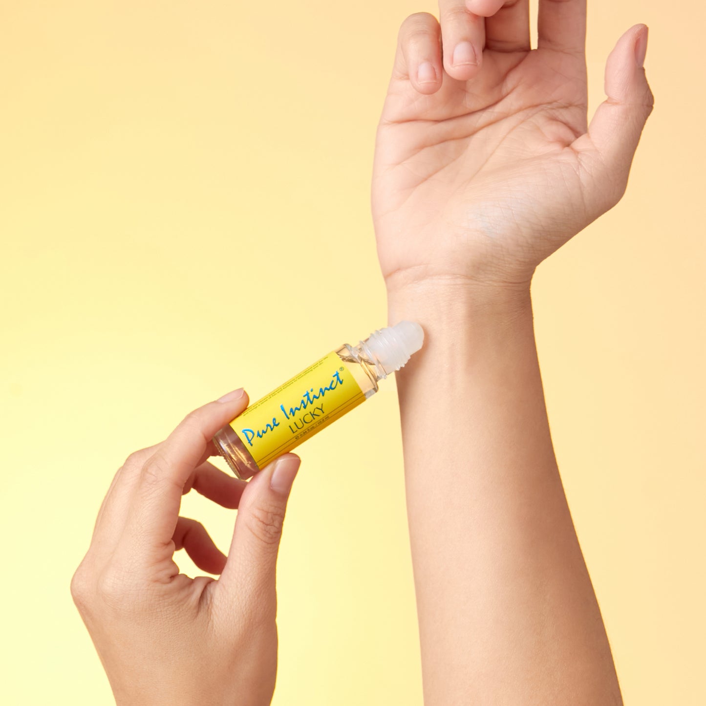 Hand applying Lucky Roll-On Pheromone Perfume Oil on wrist with a soft yellow gradient background.