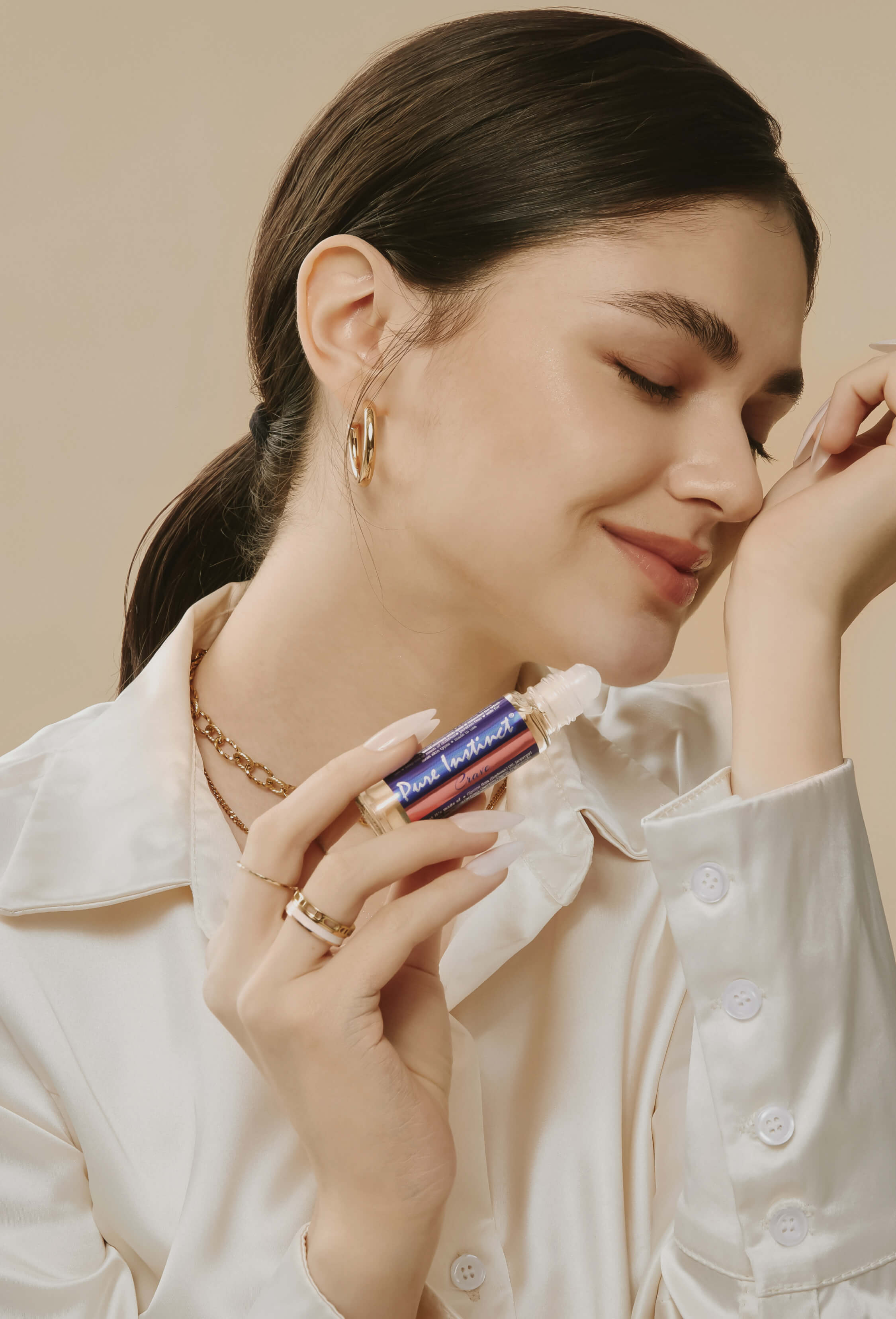 A smiling woman gently applying Pure Instinct Crave roll-on pheromone perfume oil on her wrist, enjoying the fragrance with eyes closed.