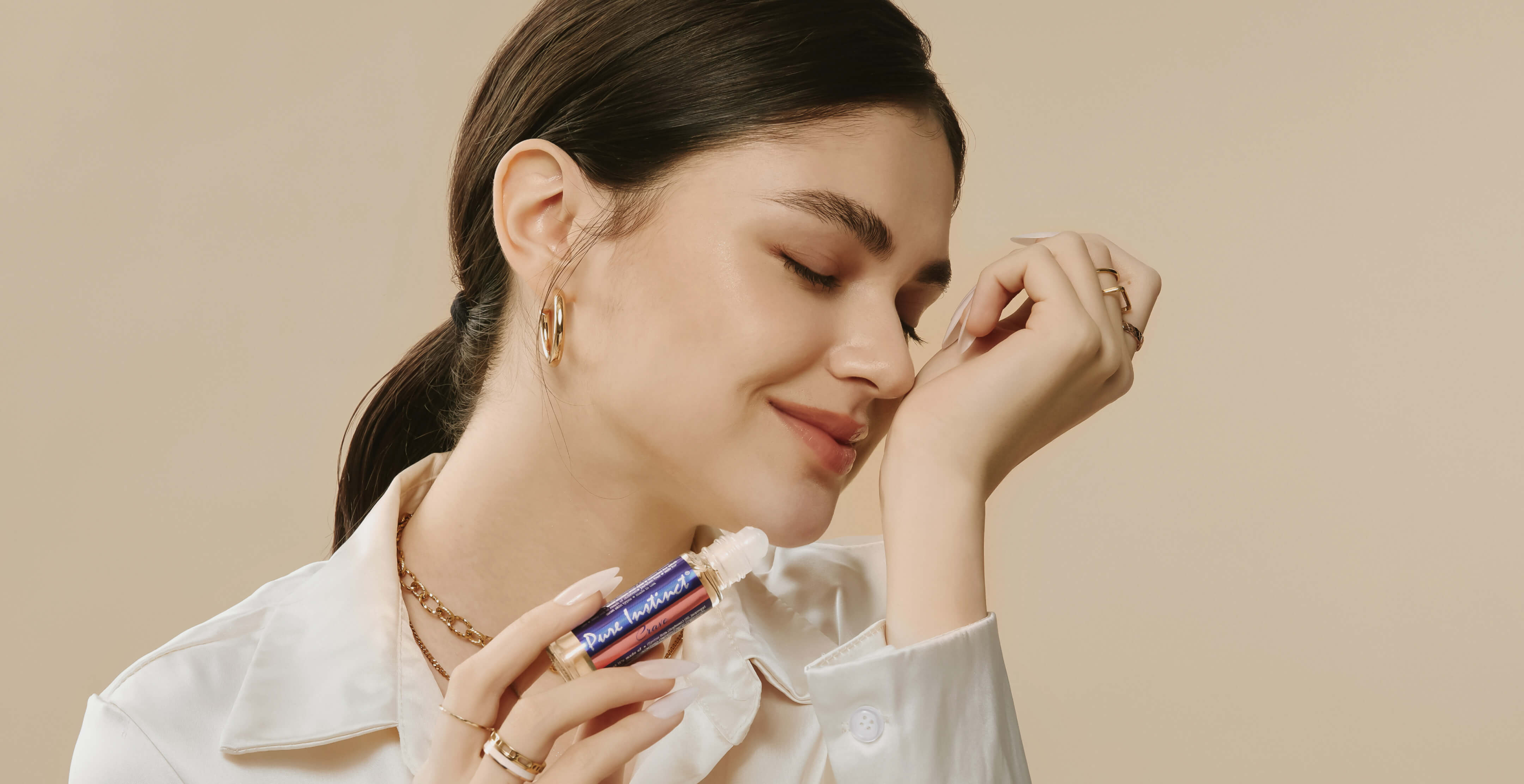 A smiling woman gently applying Pure Instinct Crave roll-on pheromone perfume oil on her wrist, enjoying the fragrance with eyes closed.