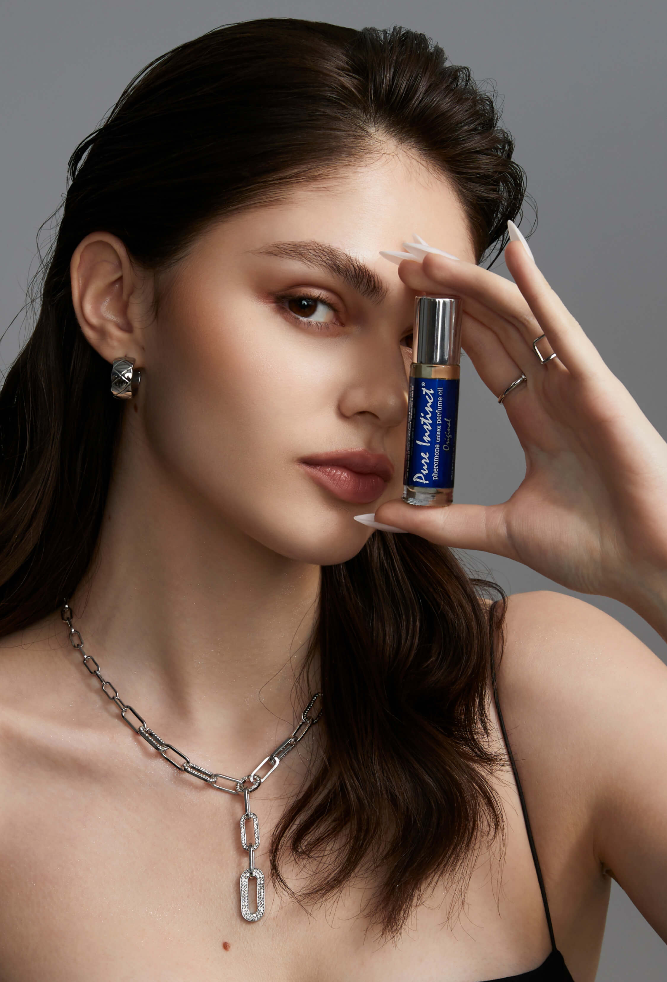 Model holding Pure Instinct Original roll-on pheromone perfume near her face.