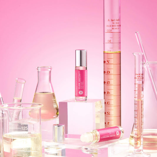 FOR HER Roll-On Pheromone Perfume Oil showcased among scientific glassware and pink-toned liquids, emphasizing the fragrance’s formulation and modern allure.