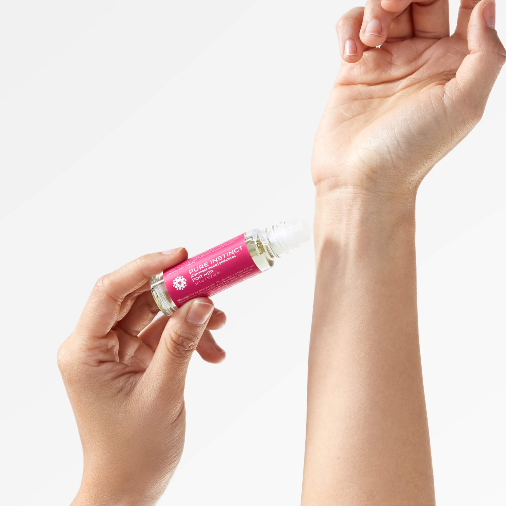 Close-up of hands applying FOR HER Roll-On Pheromone Perfume Oil to the wrist using the roll-on applicator, highlighting ease of use and personal fragrance ritual.