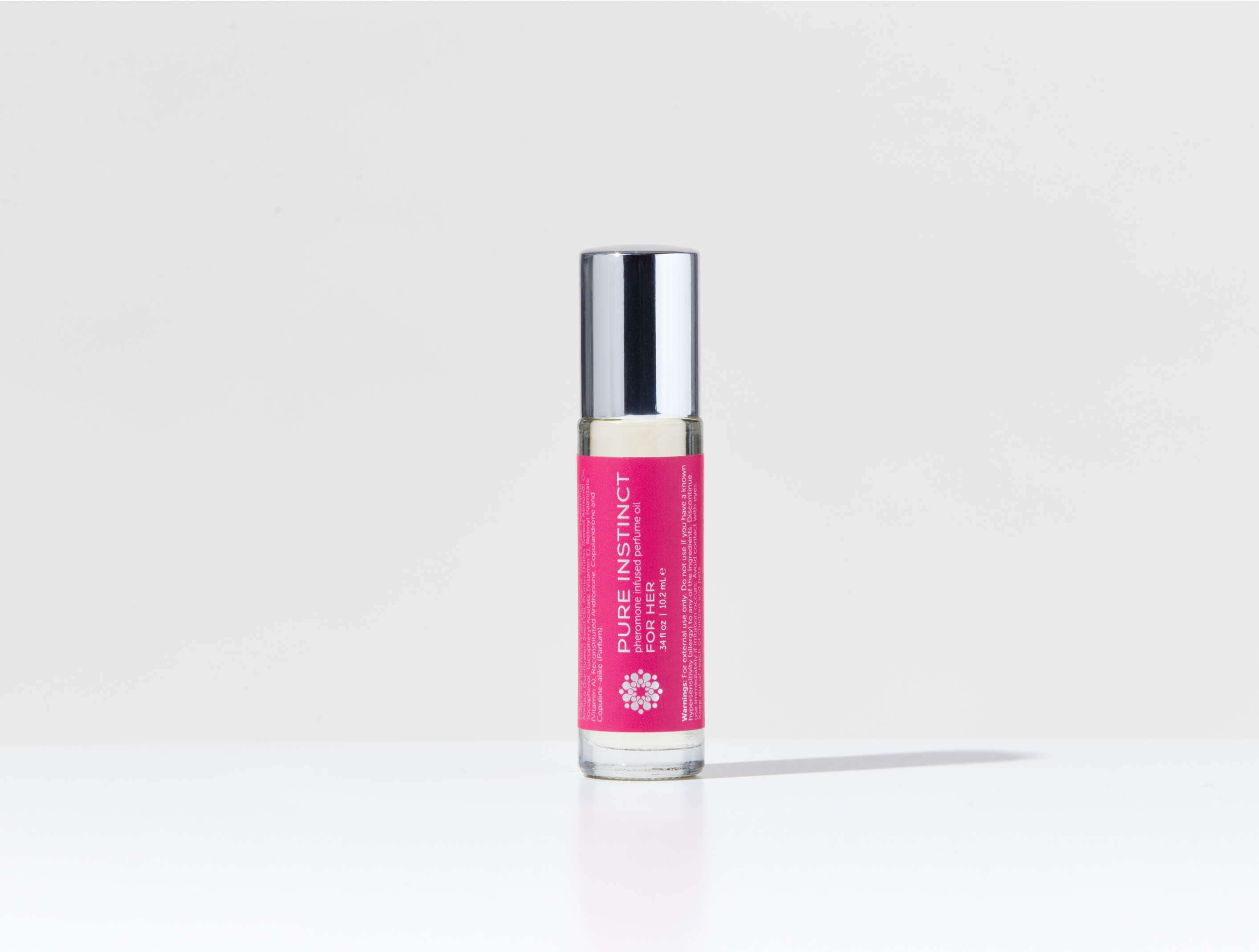 Multiple bottles of FOR HER Roll-On Pheromone Perfume Oil arranged on a soft pink background, featuring the sleek silver cap and signature magenta label design.