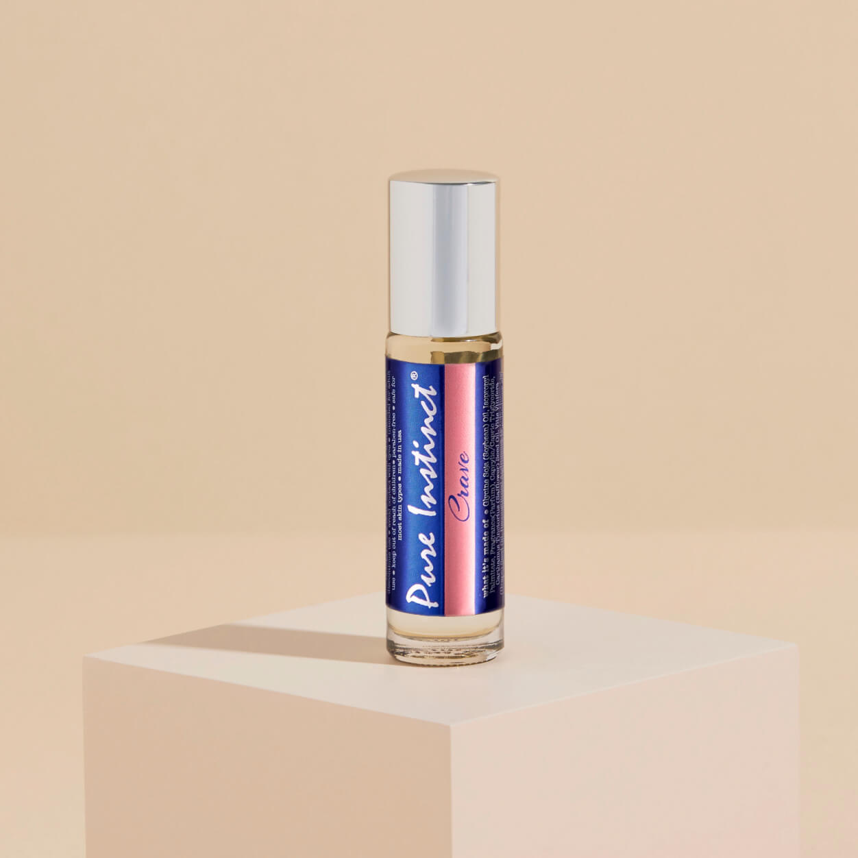 Pure Instinct Crave Roll-On Pheromone Perfume Oil standing elegantly on a soft-toned pedestal, showcasing its sleek design and bold gradient label.