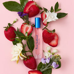 Pure Instinct Fallen perfume spray surrounded by strawberries, white flowers, and lush green leaves on a pastel pink background
